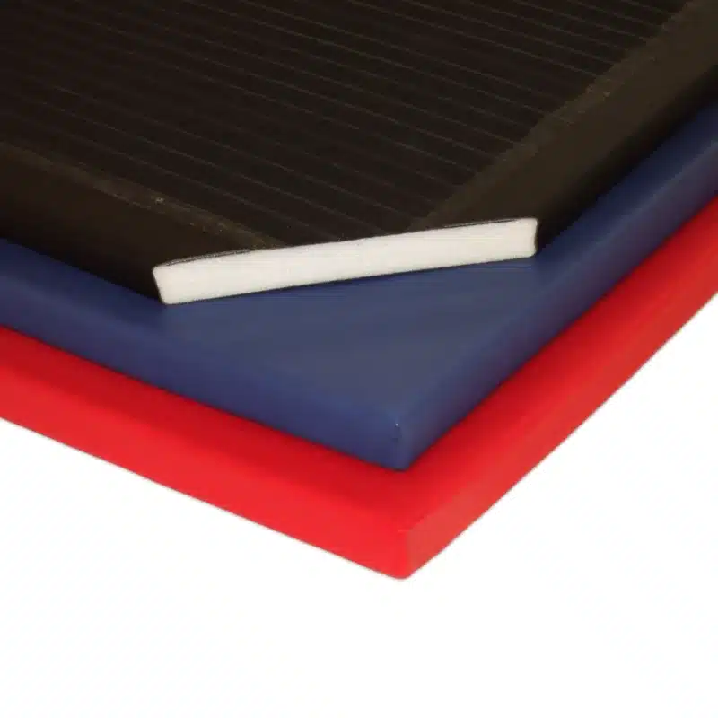 Close-up of stacked Lightweight Gym Mats in red, blue and black, showing the white polyethylene core and smooth PVC cover.