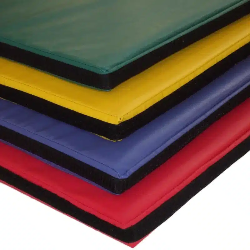 Stacked colourful play mats in green, yellow, blue and red, showing velcro edges for linking together.